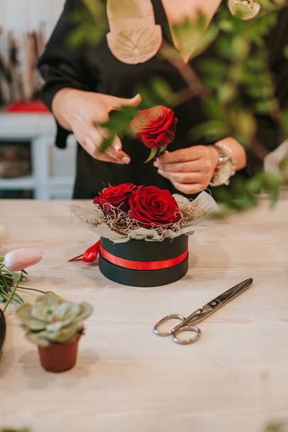 Primer plano de las manos de la florista mujer, dueño de la floristería de la pequeña empresa, en el mostrador, trabajando con rosas rojas, haciendo arreglos
. - Foto, Imagen