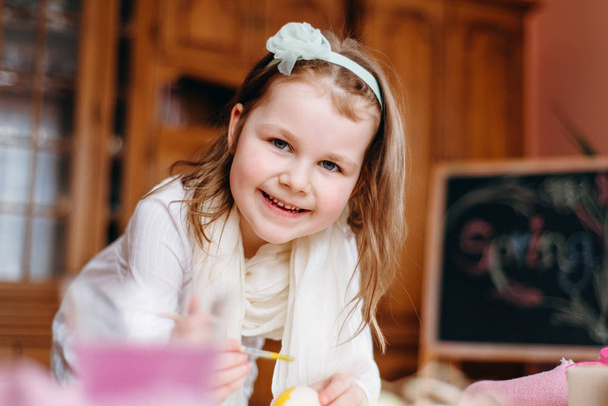 Άποψη του χαμογελαστό κοριτσάκι που φοράει στεφάνη, λευκό φόρεμα και μαντίλι κρατώντας πινέλο στο χέρι - Φωτογραφία, εικόνα
