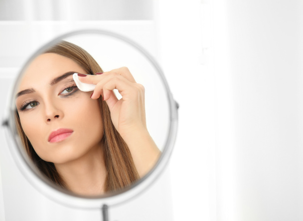 Young woman removing makeup in front of mirror indoors. Eyelash loss problem - Foto, Imagem