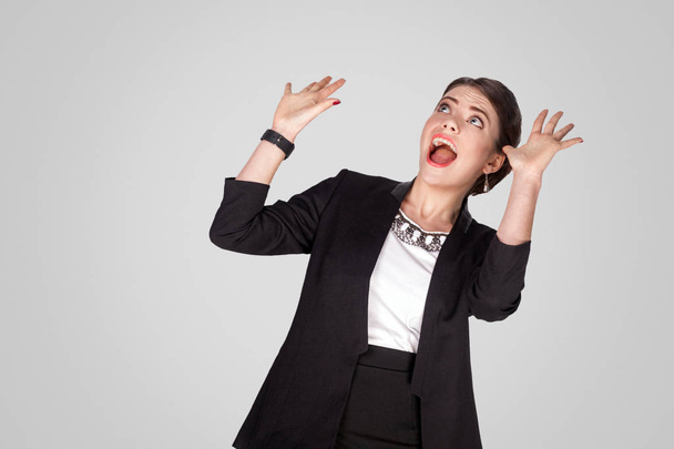 shocked woman with raised hands looking up and shouting on grey background - Foto, afbeelding