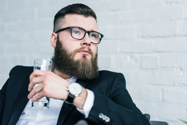 portrait of pensive businessman with glass of water in hand looking away - Photo, image