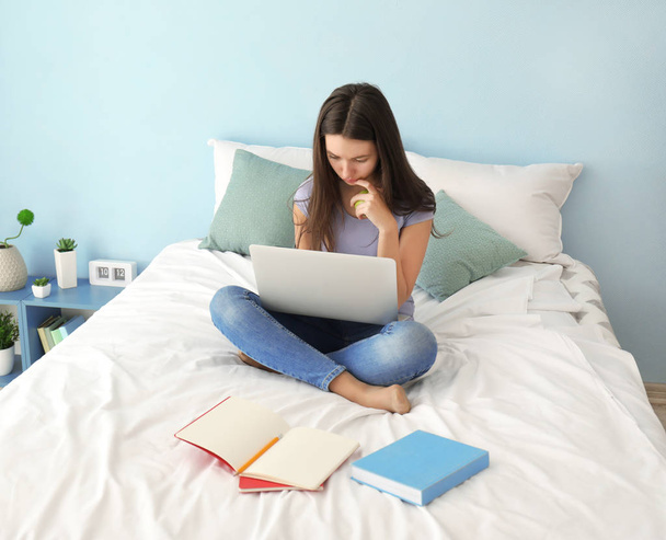 Cute teenager girl using laptop while doing homework in bedroom - Valokuva, kuva