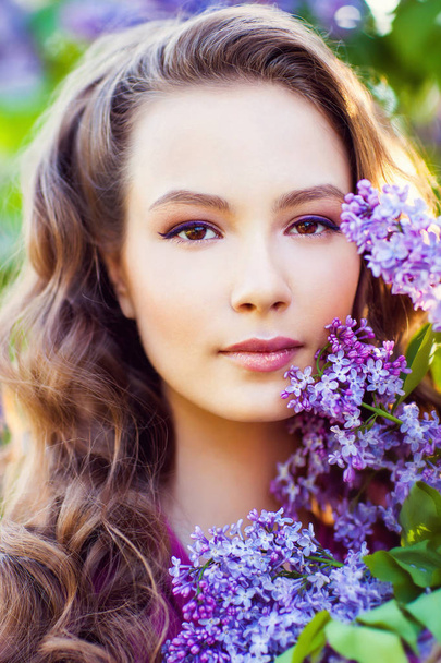 Молодая красивая девушка позирует возле лиловых кустов в цвету
 - Фото, изображение
