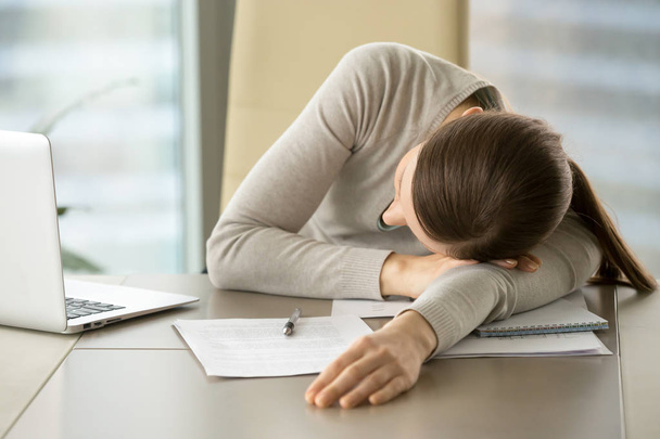 müde Büroangestellte, die wegen Überlastung mit Laptop und Geschäftsunterlagen auf dem Schreibtisch liegt. Erschöpft von harter Papierkram Geschäftsfrau schläft am Arbeitsplatz, macht am Arbeitstag ein kurzes Nickerchen - Foto, Bild
