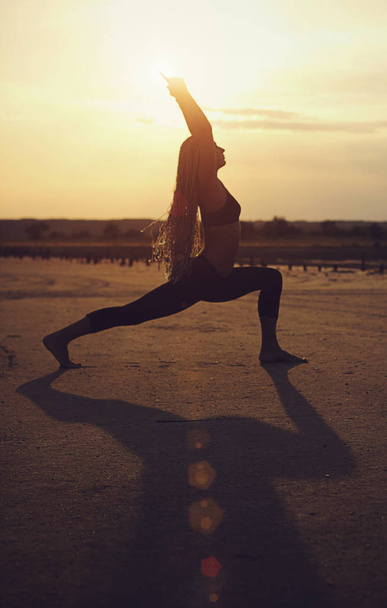 Girl in the desert at sunset is engaged in yoga in the pose of a - 写真・画像