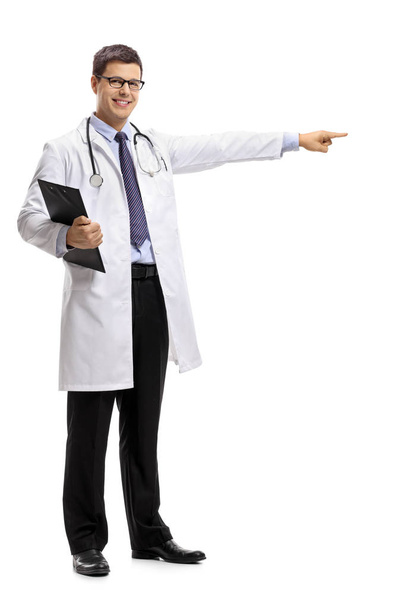 Full length portrait of a doctor with a clipboard pointing isolated on white background - Фото, изображение