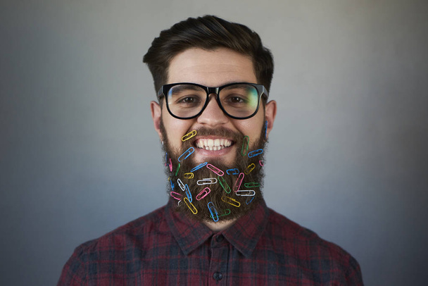 Портрет красивого мужчины в очках, скрепки в бороде на сером фоне
 - Фото, изображение
