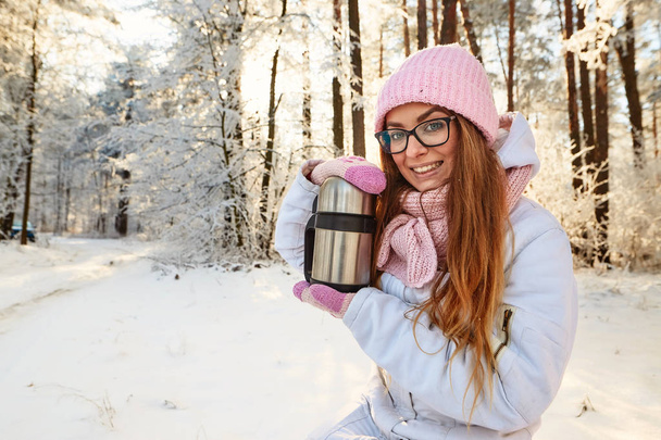 girl in a pink hat with a thermos in the winter in the forest. - Photo, Image