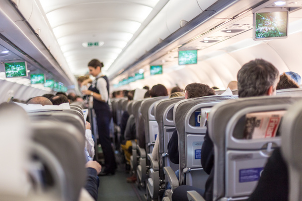 Interior del avión comercial con azafata sirviendo pasajeros en asientos durante el vuelo
. - Foto, imagen
