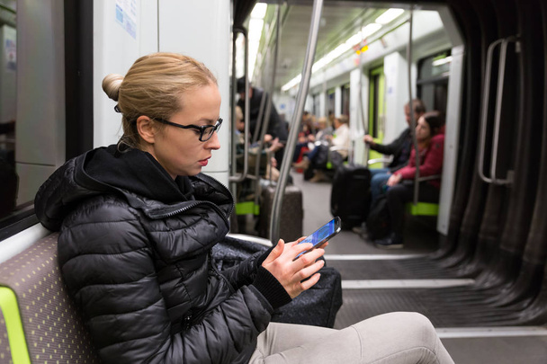 Νεαρό κορίτσι ανάγνωση από την οθόνη του κινητού τηλεφώνου στο μετρό. - Φωτογραφία, εικόνα