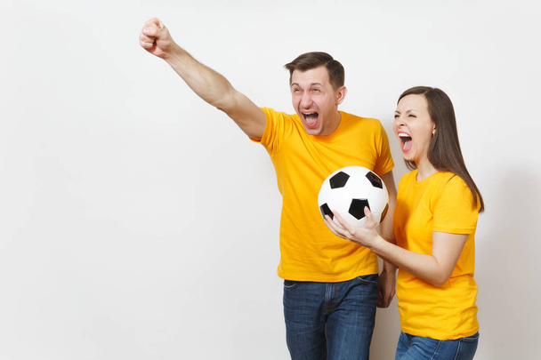 Весела весела емоційна молода пара, жінка, чоловік, шанувальники футболу в жовтій формі підбадьорюють команду підтримки з футбольним м'ячем ізольовано на білому тлі. Спорт, сімейне дозвілля, концепція способу життя
. - Фото, зображення