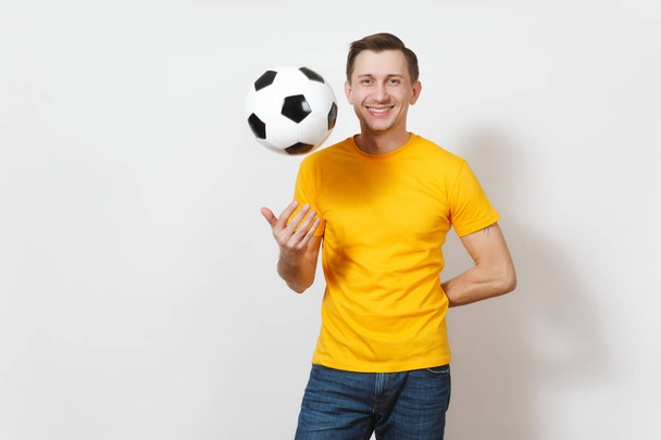 Geïnspireerd vrolijke Europese jongeman, ventilator of speler in geel uniform gooien van voetbal, cheer favoriete voetbalteam geïsoleerd op een witte achtergrond. Sport, voetballen, gezonde levensstijl concept. - Foto, afbeelding