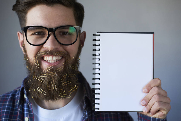 Ritratto di bell'uomo sorridente con graffette in barba che mostrano carta bianca vuota su sfondo grigio
 - Foto, immagini