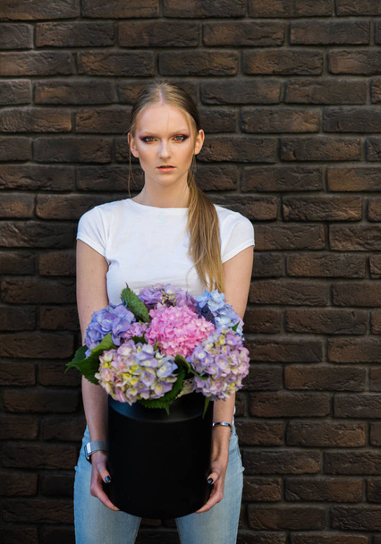 Woman hold vase with hydrangea flowers on brick wall - 写真・画像