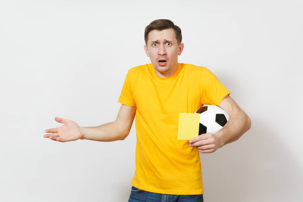 European sad upset crying shocked young man, football fan or player in yellow uniform hold in hand yellow soccer card for retire from field isolated on white background. Sport play, lifestyle concept. - Photo, Image