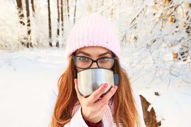Mädchen mit rosa Hut trinkt im Winter im Wald Tee aus der Thermoskanne. - Foto, Bild