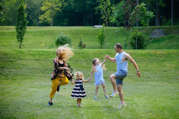 Girls, woman and man smile on summer landscape. Children and parents jump on green grass. Happy childhood, family, love. Mothers and fathers day. Freedom, activity, lifestyle, energy concept. - Photo, Image