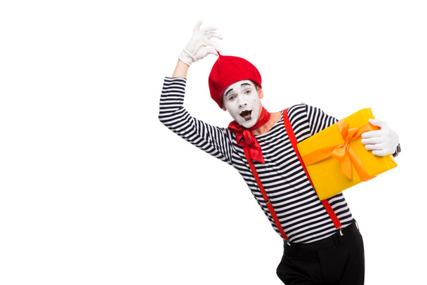 surprised mime holding gift box and touching red cap isolated on white - Photo, Image
