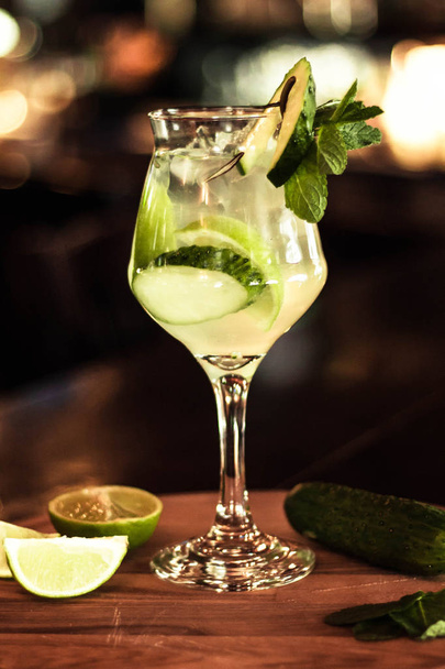 delicious cocktail with lime, cucumber and mint leaves in wineglass on wooden table in bar  - Foto, imagen
