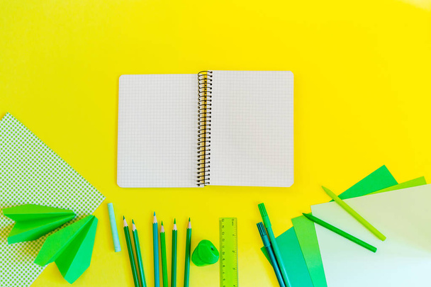 kreative, modische, minimalistische, Schul- oder Büroarbeitsplätze mit grünem Material auf gelbem Hintergrund. flach lag. Spiralheft auf gelbem Hintergrund. - Foto, Bild
