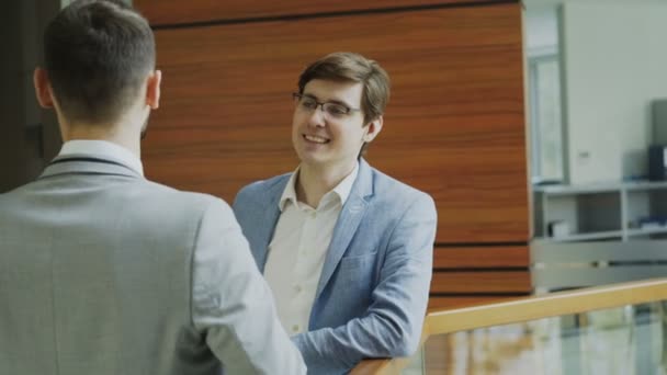 Two businessman colleagues standing and chatting standing near railing in hall of modern business center - Filmagem, Vídeo