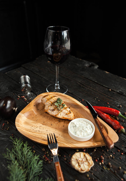 Jugoso filete de pollo a la parrilla en un plato de madera con una copa de vino tinto
 - Foto, imagen