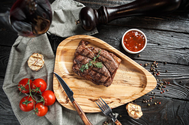 piękny porcja mięsa stek na drewnianej tablicy z Sałatka, sos pomidorowy i kieliszek czerwonego wina na ciemnym tle drewnianych - Zdjęcie, obraz