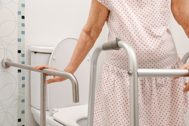 Elderly woman holding on handrail in toilet. - Photo, Image