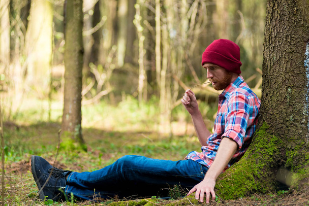 Πορτραίτο ενός άνδρα σε ένα καπάκι και το καρό πουκάμισο που κάθονται κοντά σε ένα δέντρο μου - Φωτογραφία, εικόνα