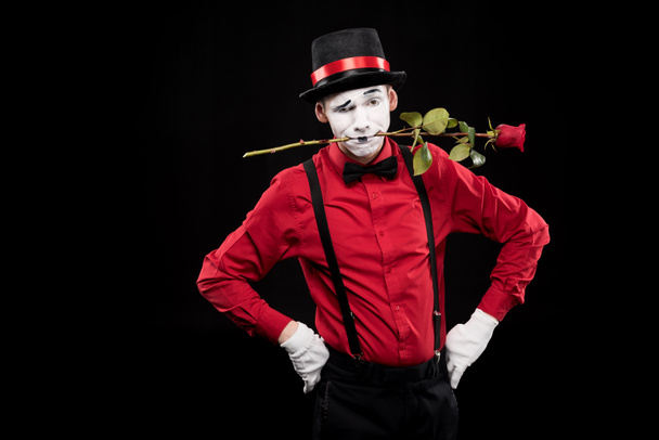 mime grimacing and holding red rose in mouth isolated on black - Foto, Imagem