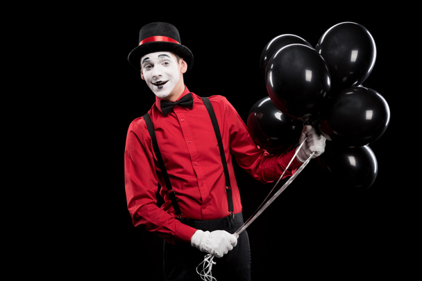 χαμογελώντας mime κρατώντας δέσμη μαύρα μπαλόνια που απομονώνονται σε μαύρο - Φωτογραφία, εικόνα