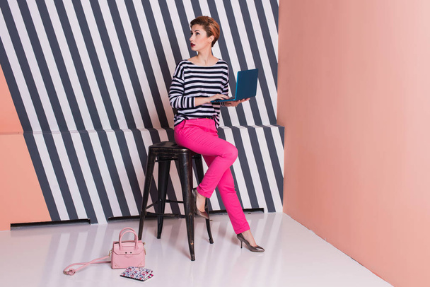 Stylish woman with a laptop in her hands in a striped T-shirt and pink pants, lifestyle, blogger, business, online shopping - Foto, imagen