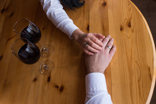 The hand of a man with a ring stretches to the woman's hand. Two glasses with red wine. Romantic dinner, a date. The hand of couple in love with wedding rings - Фото, зображення