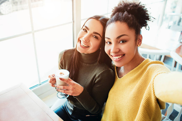 This is a selfie of two beautiful girls that look so amazing and happy at the same time. They are in cafe drinking some coffee end enjoying time spending together. Close up. Cut view. - Foto, immagini
