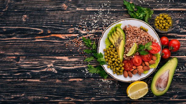 Healthy food. Buckwheat, cherry tomatoes, avocados, almonds and green peas. On a wooden background. Top view. Free space for your text. - 写真・画像