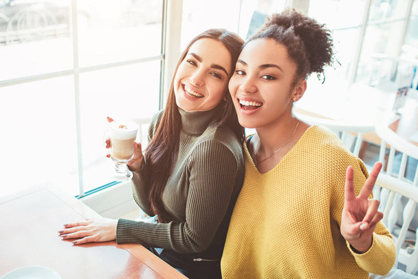 This is a selfie of two beautiful girls that look so amazing and happy at the same time. They are in cafe drinking some coffee end enjoying time spending together. Close up. Cut view. - Photo, Image