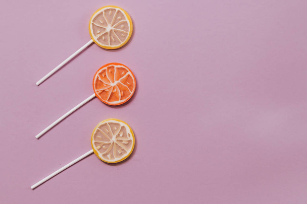 three sweet citrus lollipops on lilac background - Photo, Image