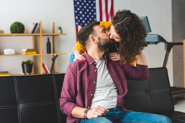 Man kissing girlfriend while sitting on leather sofa - Фото, изображение