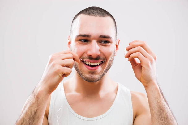 Νεαρός άνδρας χρησιμοποιώντας οδοντικό νήμα για να καθαρίσετε τα δόντια του.  - Φωτογραφία, εικόνα