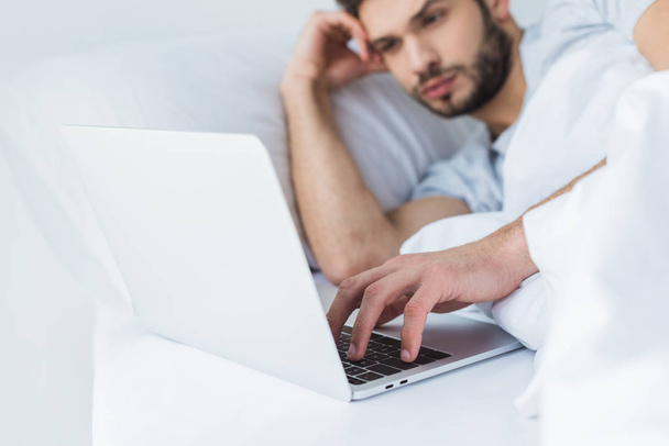 selective focus of man lying on bed and using laptop - Φωτογραφία, εικόνα