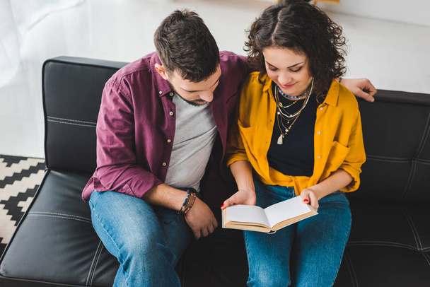 High angle view of young couple sitting on couch and reading book - Photo, Image