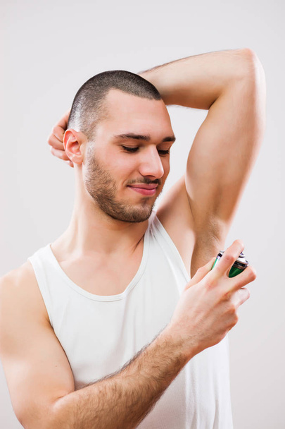Young man is applying antiperspirant to his armpit.  - Photo, Image