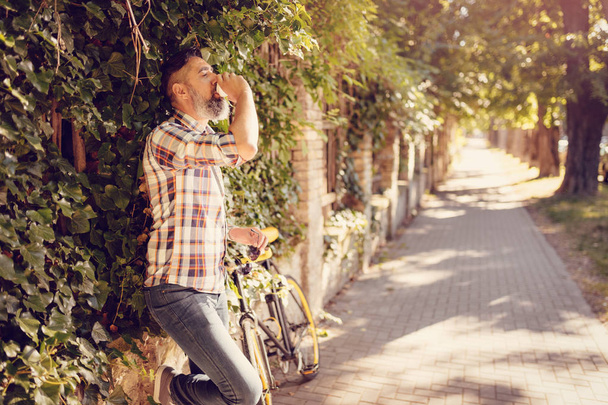 Случайный бизнесмен пьет кофе, чтобы пойти и стоять у стены рядом с велосипедом
. - Фото, изображение