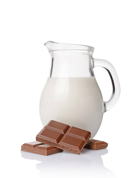 Close-up pieces of chocolate bar with glass jug of milk - Фото, зображення