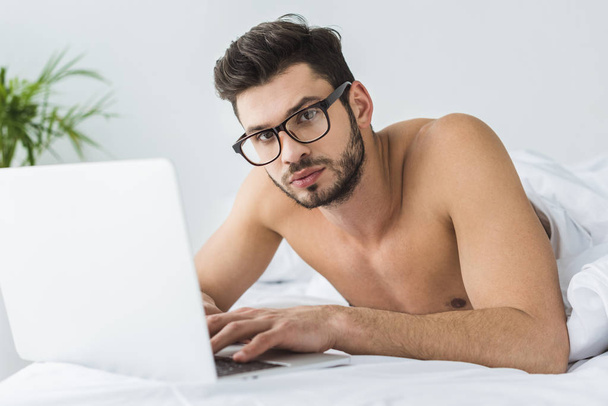 jóképű férfi szemüveg használ laptop az ágyban reggel - Fotó, kép