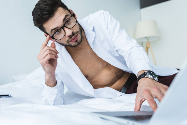 hombre de negocios barbudo en gafas usando portátil en la cama por la mañana
 - Foto, Imagen