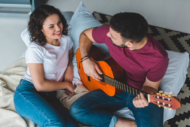 Mann spielt auf Akustikgitarre, Freundin liegt daneben - Foto, Bild