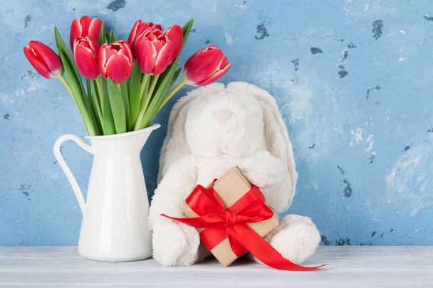Czerwone tulipany w dzban, Pudełko prezentowe i królik zabawki przed mur. - Zdjęcie, obraz