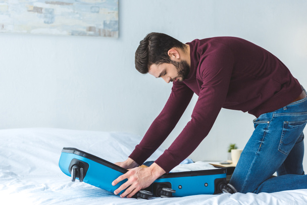 handsome man packing baggage on bed for trip - Photo, Image