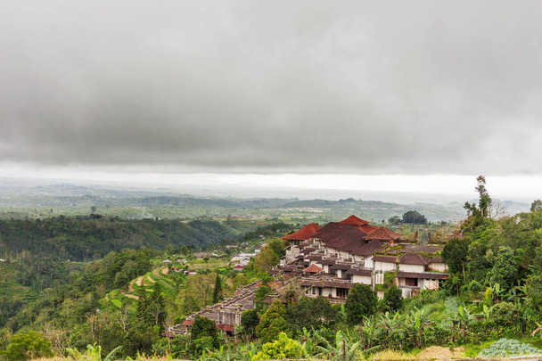 Panorama view on building in village and agricultural rice fields on hill. Winter cloudy and rainy season. Bali island, Indonesia. - Fotó, kép